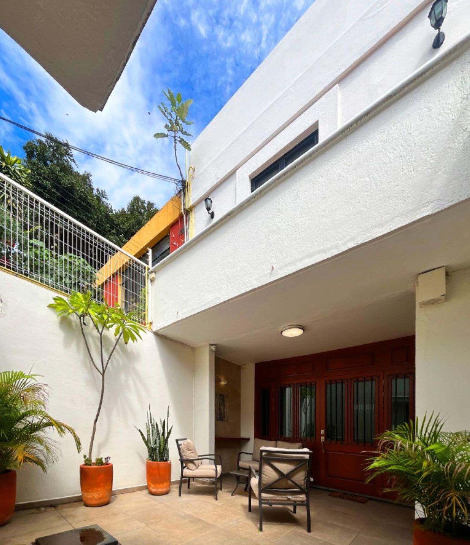 Un bâtiment à deux étages doté d’un patio couvert, aménagé avec du mobilier d’extérieur et des plantes en pot.