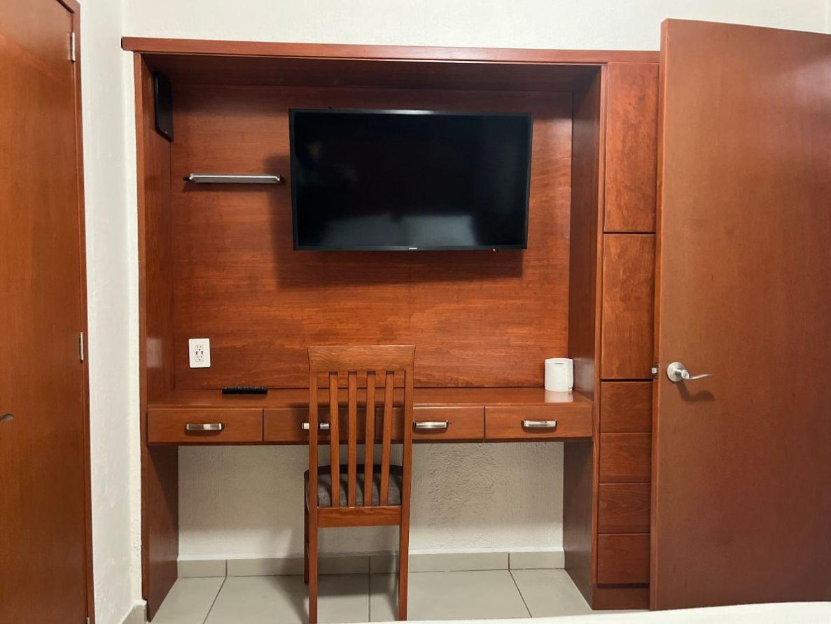 Un bureau en bois, un téléviseur à écran plat, une chaise et un meuble avec des tiroirs.