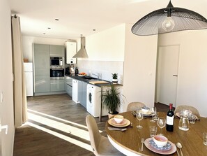 A modern kitchen with stainless steel appliances, a dining area with a round table set for six, and a large pendant light. - New Listing (Pontenx-les-Forges)