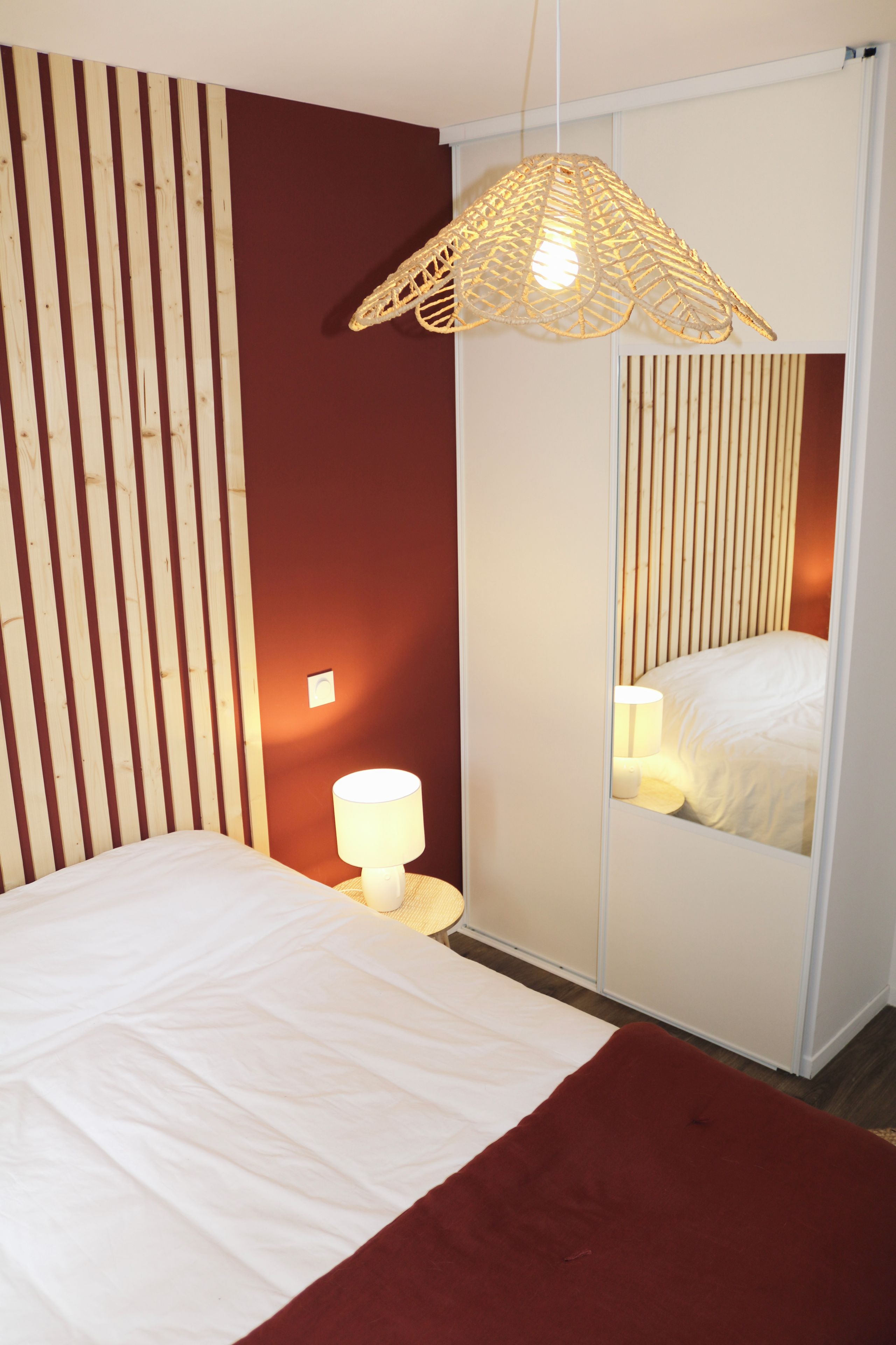 A bedroom with a bed, a bedside lamp, a mirror, and a hanging light fixture.
