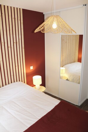 A bedroom with a bed, a bedside lamp, a mirror, and a hanging light fixture. - New Listing (Pontenx-les-Forges)
