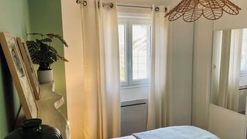 Ein Schlafzimmer mit Bett, einem Fenster mit Vorhängen, einer Pendelleuchte und einer Topfpflanze.
