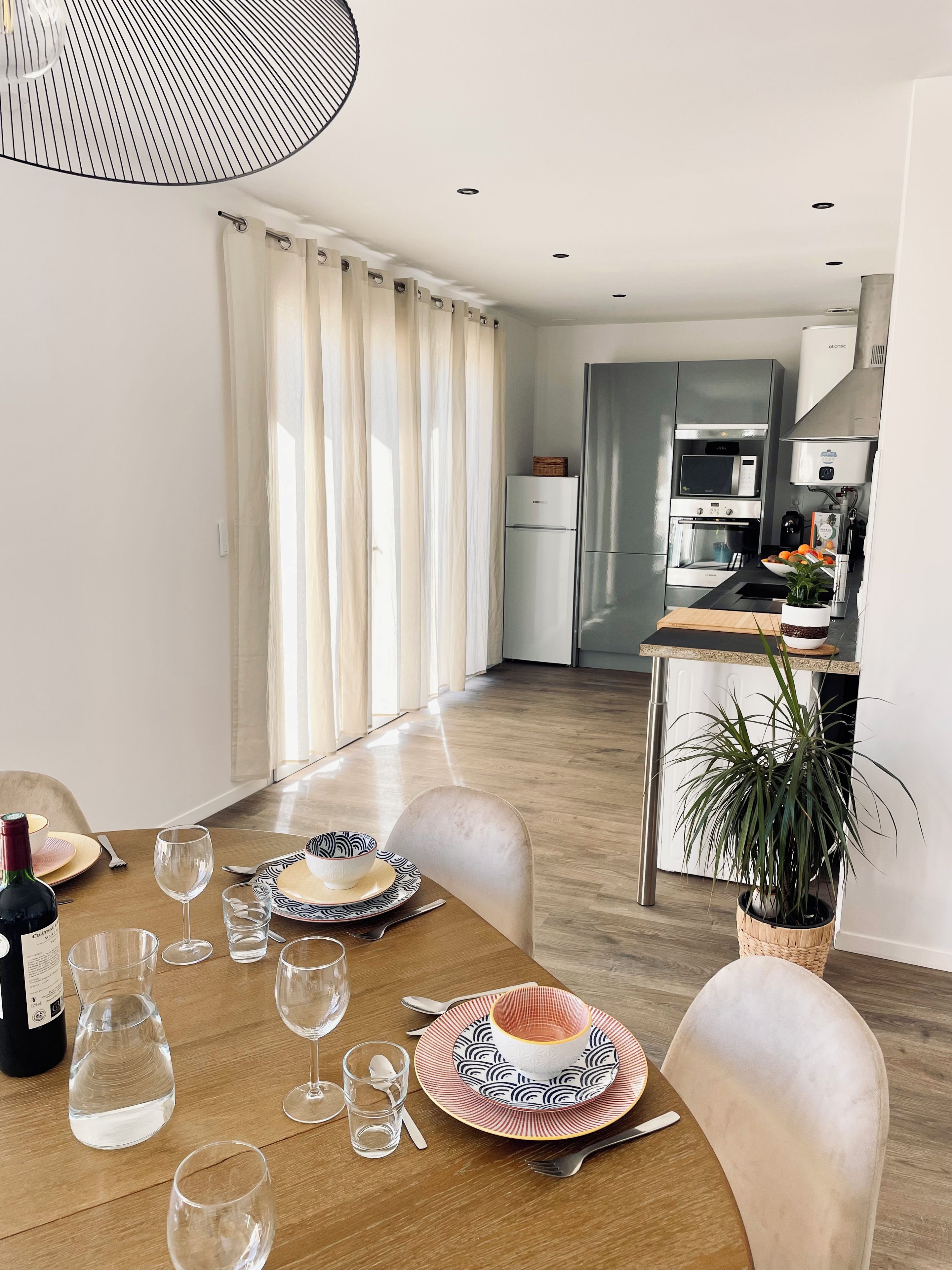 A dining area with a table set for four, a kitchen in the background, and a potted plant on the table.