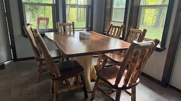 Un coin repas avec une table et des chaises en bois, de grandes fenêtres donnant sur la verdure et un sol carrelé.