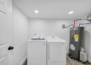 A laundry room with two white washing machines and a gray water heater.