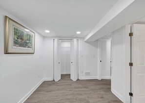 Un couloir aux murs blancs, doté d’un plancher en bois et orné d’un tableau encadré sur le côté gauche.