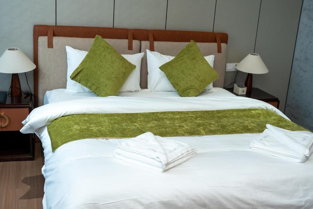 Habitación de hotel con cama, almohadas, una colcha y una mesita de noche con lámpara.