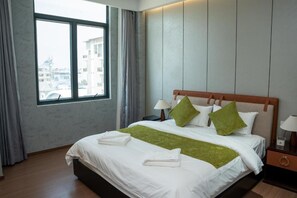 Habitación de hotel con una cama grande, dos mesitas de noche, un ventanal con cortinas y vistas a edificios.