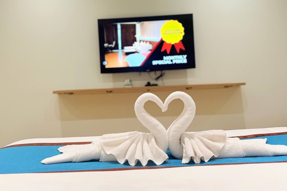 Una habitación de hotel con una cama, un televisor en la pared y una decoración con forma de corazón sobre la cama.