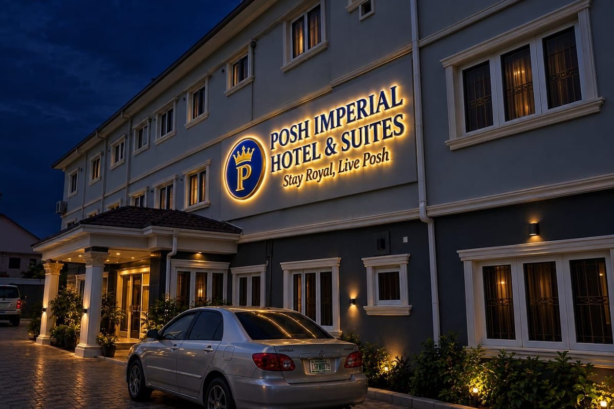 L’entrée d’un hôtel, avec une enseigne indiquant « Posh Imperial Hotel & Suites » et une voiture garée.
