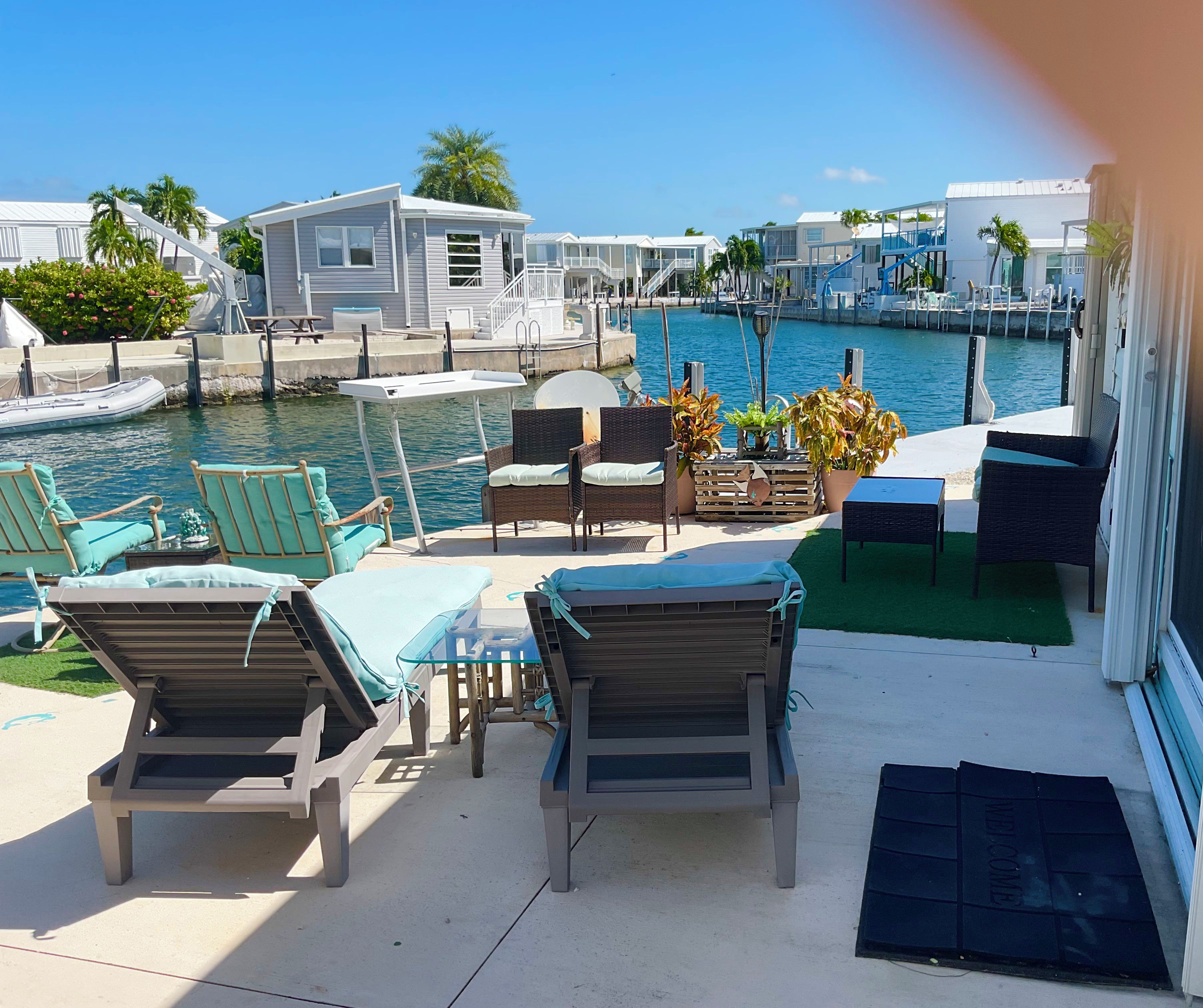 A waterfront patio with lounge chairs, a table, and a view of the marina.