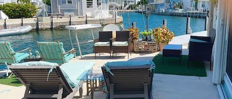 A waterfront patio with lounge chairs, a table, and a view of the marina.