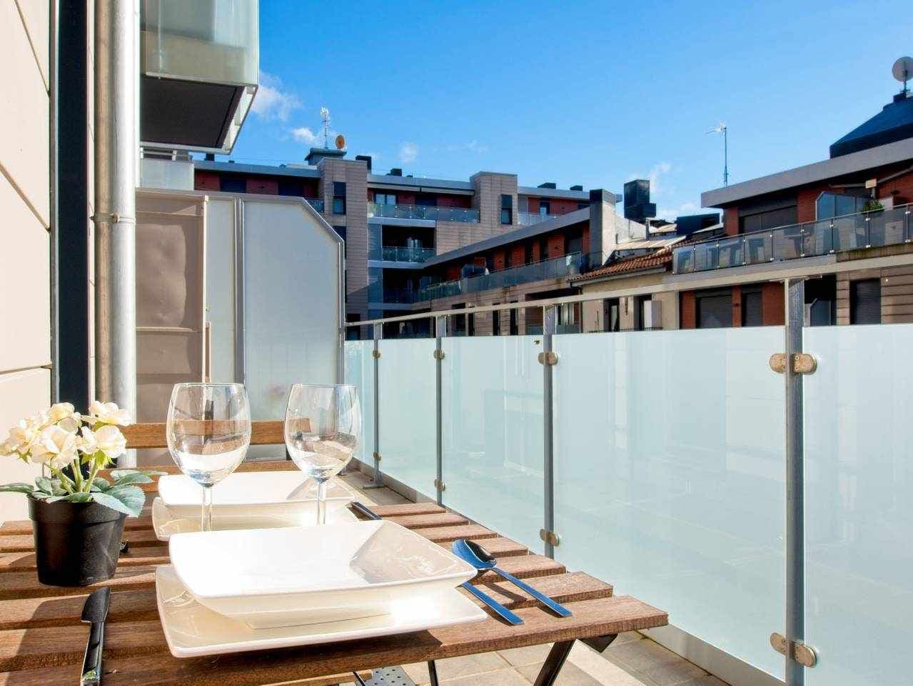 Ein Tisch auf einem Balkon mit Blick auf die Stadt, ein Blumentopf und zwei Weingläser.