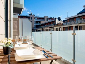 Una mesa en un balcón con vistas a la ciudad, una planta en maceta y dos copas de vino.