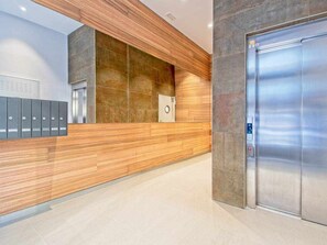 Zona de recepción con mostrador de madera, una caja fuerte empotrada, un conjunto de taquillas y un moderno ascensor.