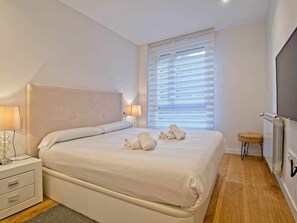Una habitación de hotel con una cama, lámparas de noche, un radiador y una ventana con persianas.