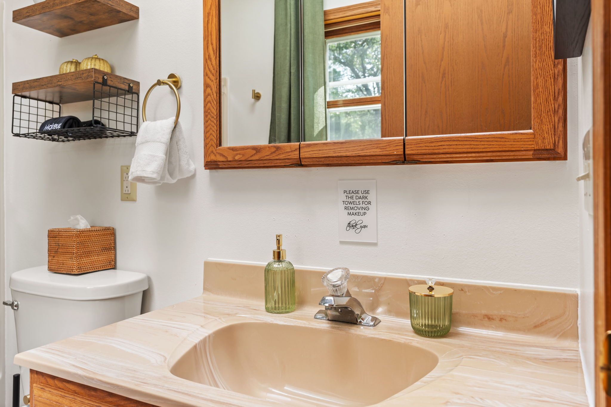 A bathroom with a marble sink, a wooden vanity, a towel rack, and a sign requesting the use of dark towels for makeup removal.