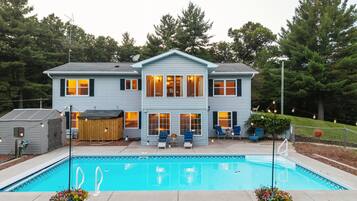 Une maison à deux étages avec une piscine, un espace salon extérieur et une cour clôturée.