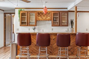 Een keuken met houten kastjes, een wit aanrecht en drie barstoelen.