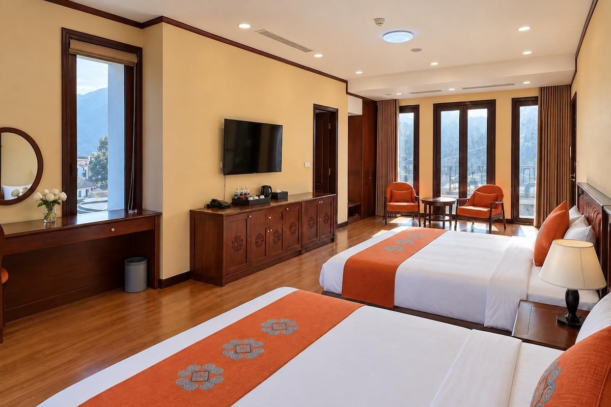 Habitación de hotel con dos camas, televisión, escritorio y vista a las montañas.