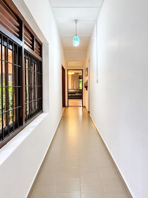 A corridor with a window on the left, a ceiling light, and a door at the end. - 4-bedroom house in Negombo close to the Airport (Negombo)