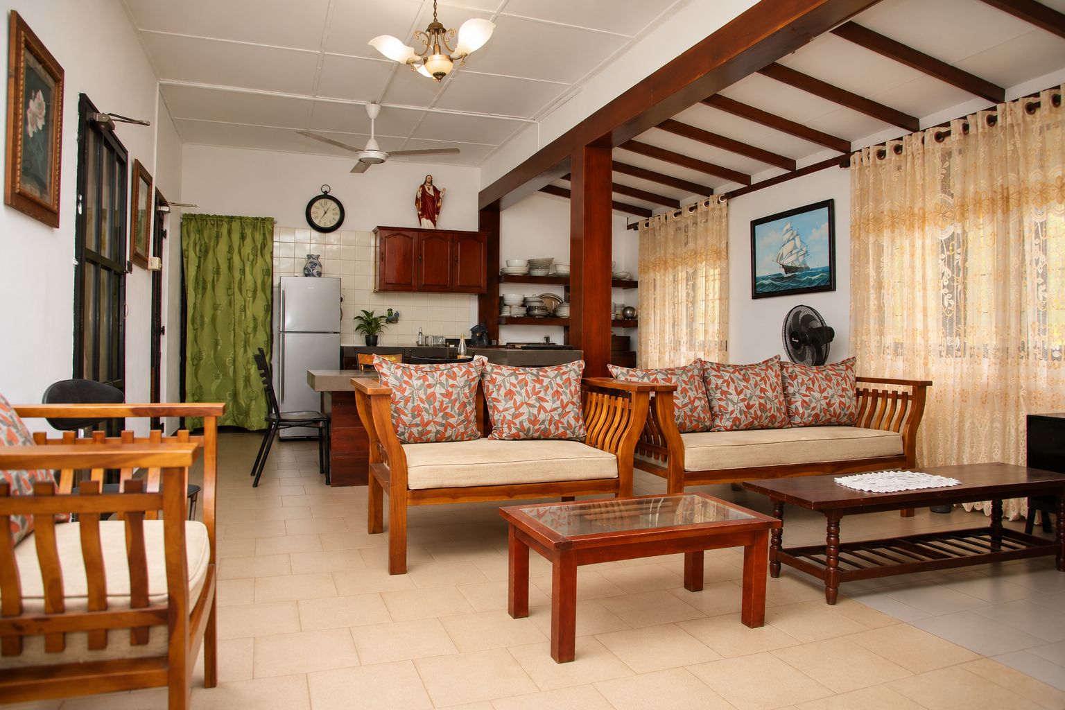 A living room with wooden furniture, a dining table, and a kitchen in the background.