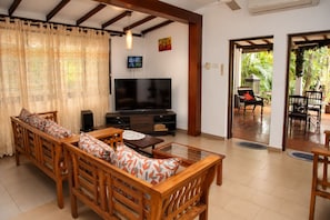 A living room with a sofa, coffee table, TV, and a view to an outdoor patio. - 4-bedroom house in Negombo close to the Airport (Negombo)