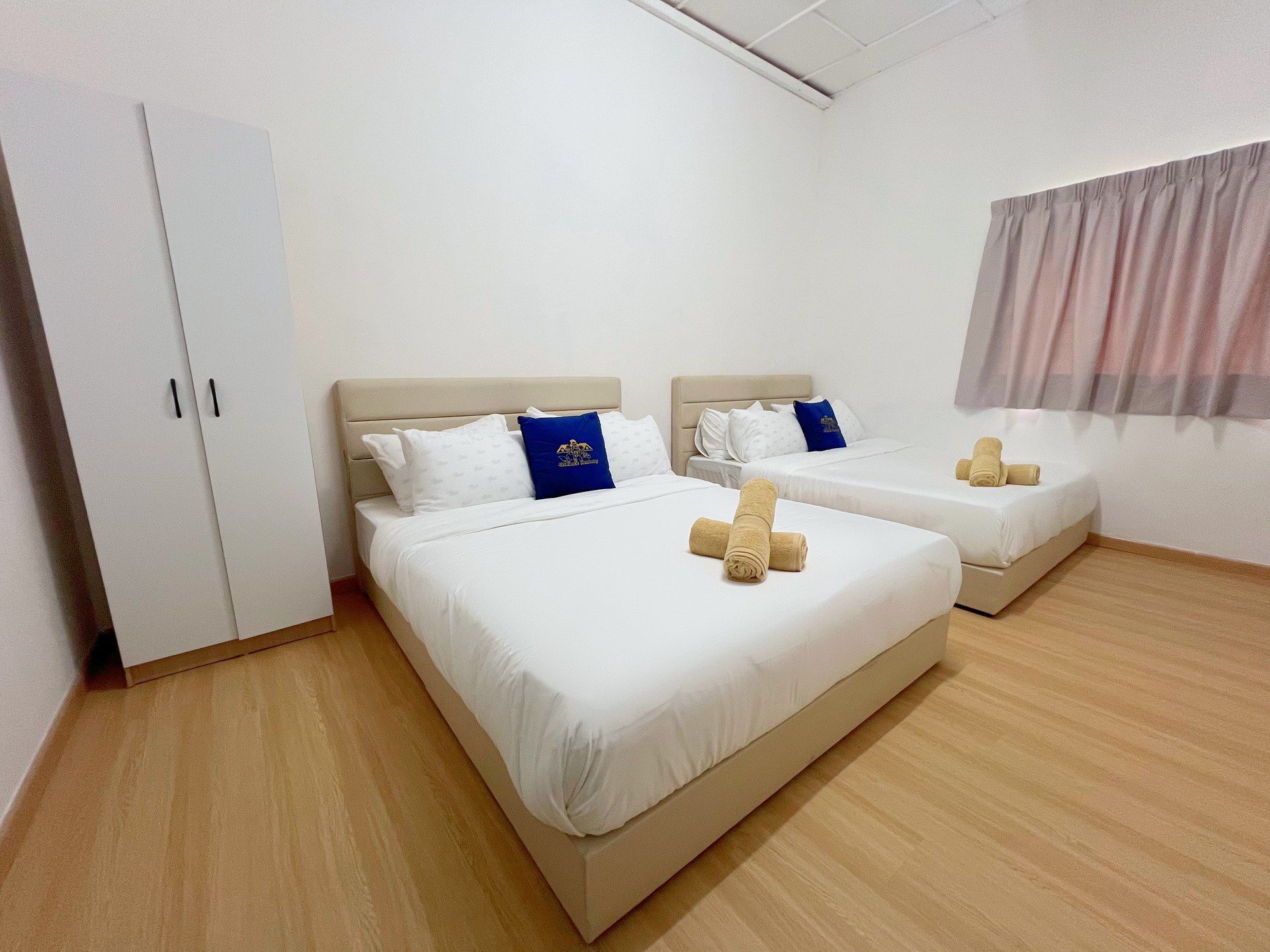 A hotel room with two beds, a wardrobe, and a window with curtains.