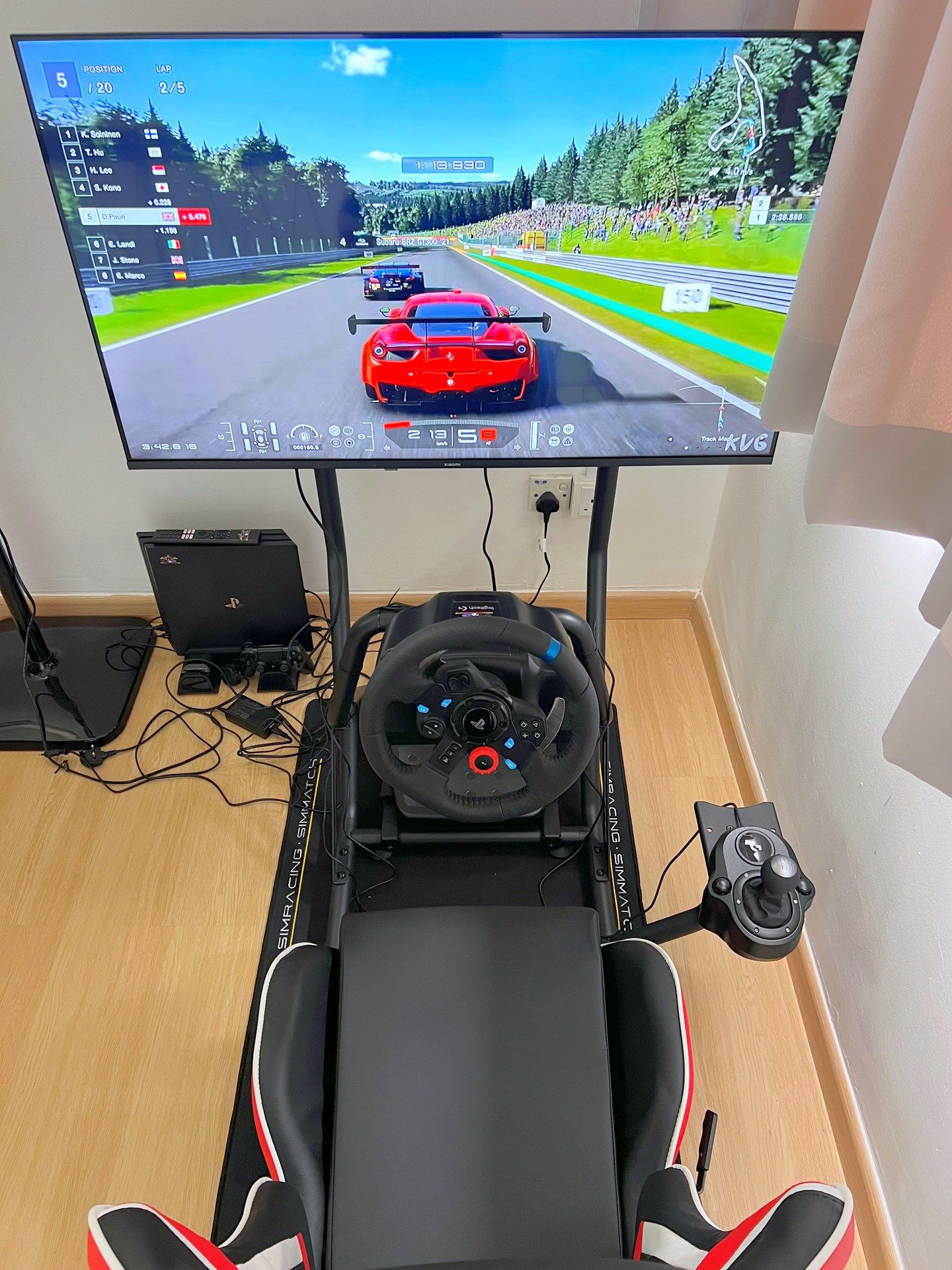 Configuração de simulador de corrida, incluindo volante, pedais e monitor exibindo um jogo de corrida.