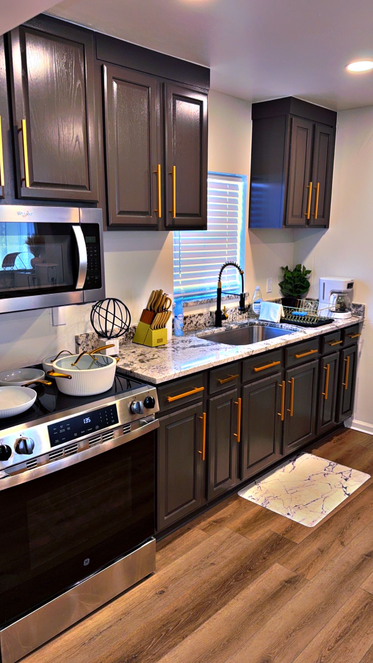 A modern kitchen with dark cabinetry, stainless steel appliances, and a marble countertop.