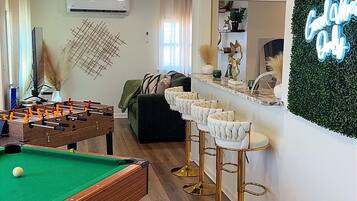 Une pièce avec une table de billard, un coin bar avec des tabourets et un néon mural.