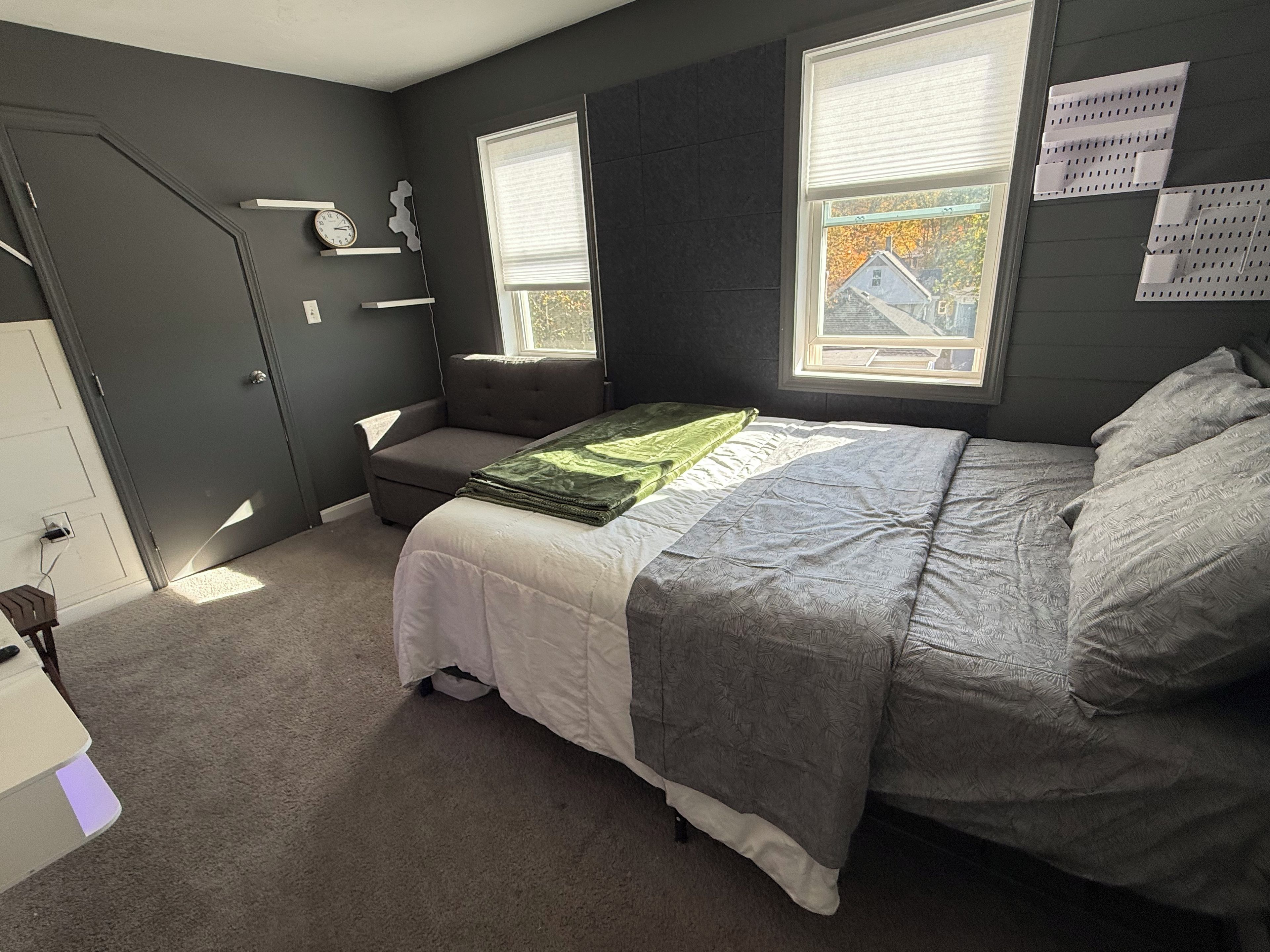 Ein Schlafzimmer mit einem Bett, einer Bank, einem Schminktisch und einem Fenster mit Jalousien.