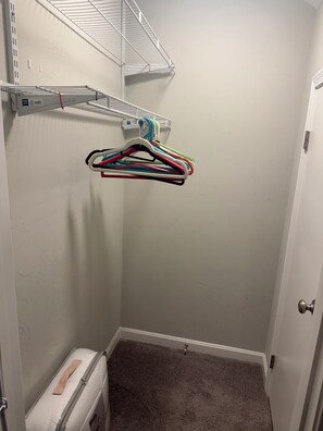 Quarto de canto com porta branca, armário pequeno branco e um cabideiro com vários ganchos coloridos.