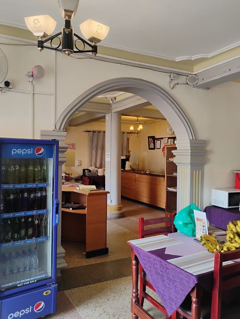A room with a dining table, chairs, a Pepsi refrigerator, and a kitchen area in the background.