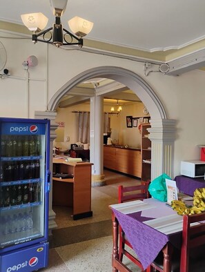A room with a dining table, chairs, a Pepsi refrigerator, and a kitchen area in the background. - Pearl Express Hotel Kabale (Kabale)