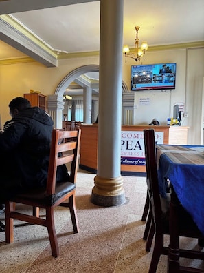 A hotel lobby with a reception desk, a television mounted on the wall, and a large pillar. - Pearl Express Hotel Kabale (Kabale)