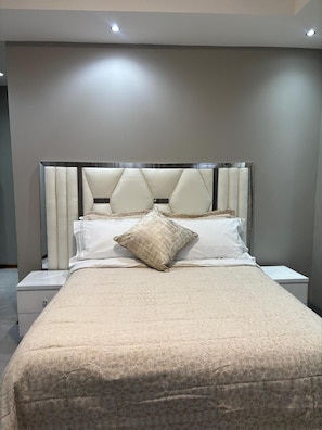 Ein modernes Schlafzimmer mit einem großen Bett, einem gepolsterten Kopfteil und einem Nachttisch.