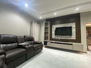 Ein modernes Wohnzimmer mit einer Ledersofa, einem flachbildfernseher, der an einer Marmorwand angebracht ist, und einer eingebauten Unterhaltungsanlage.