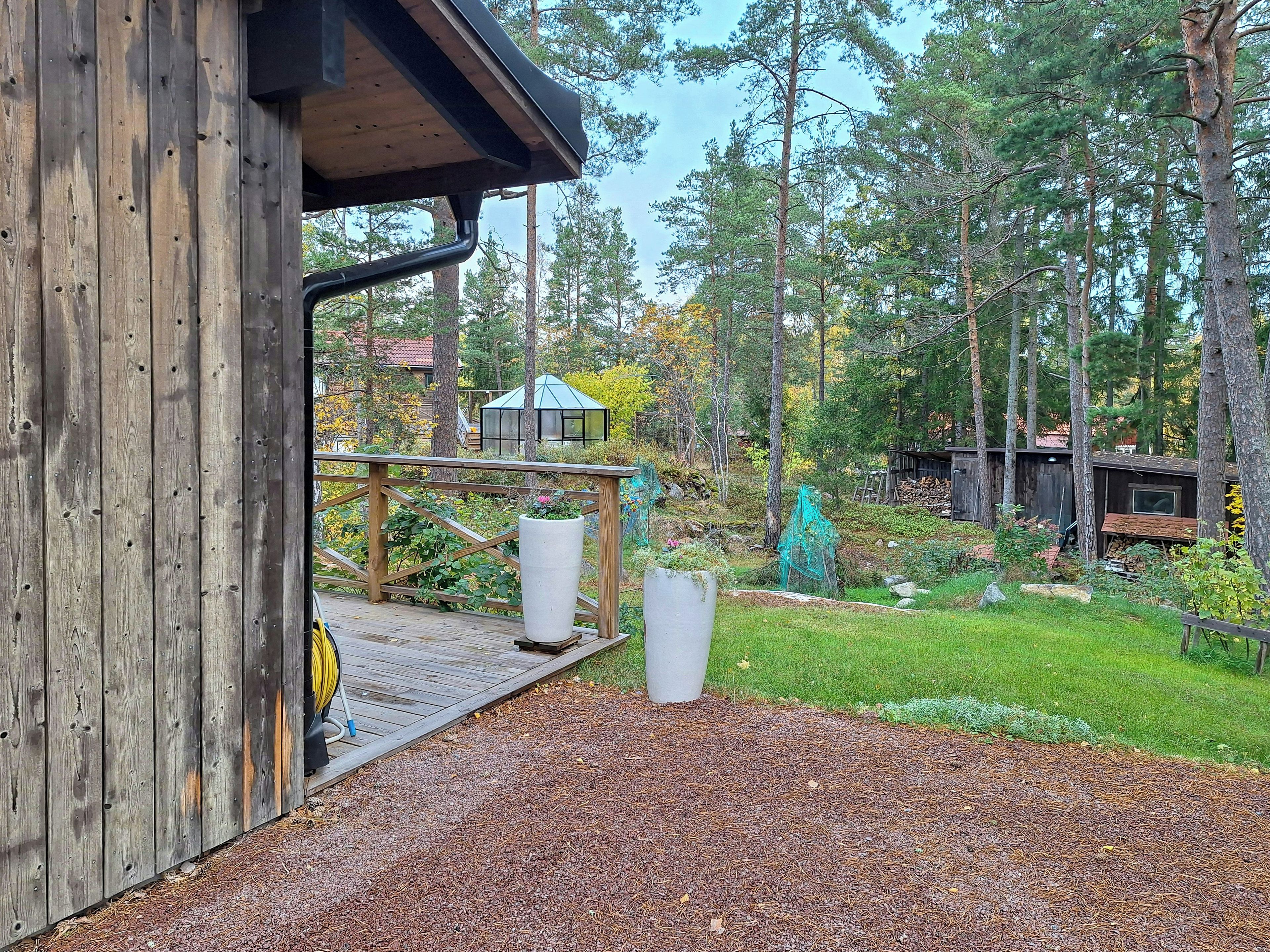 Puinen terassi, jossa on puutarhaletku, suuri kukkaruukku ja huvimaja metsäisellä alueella.