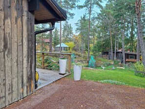 Puinen terassi, jossa on puutarhaletku, suuri kukkaruukku ja huvimaja metsäisellä alueella.