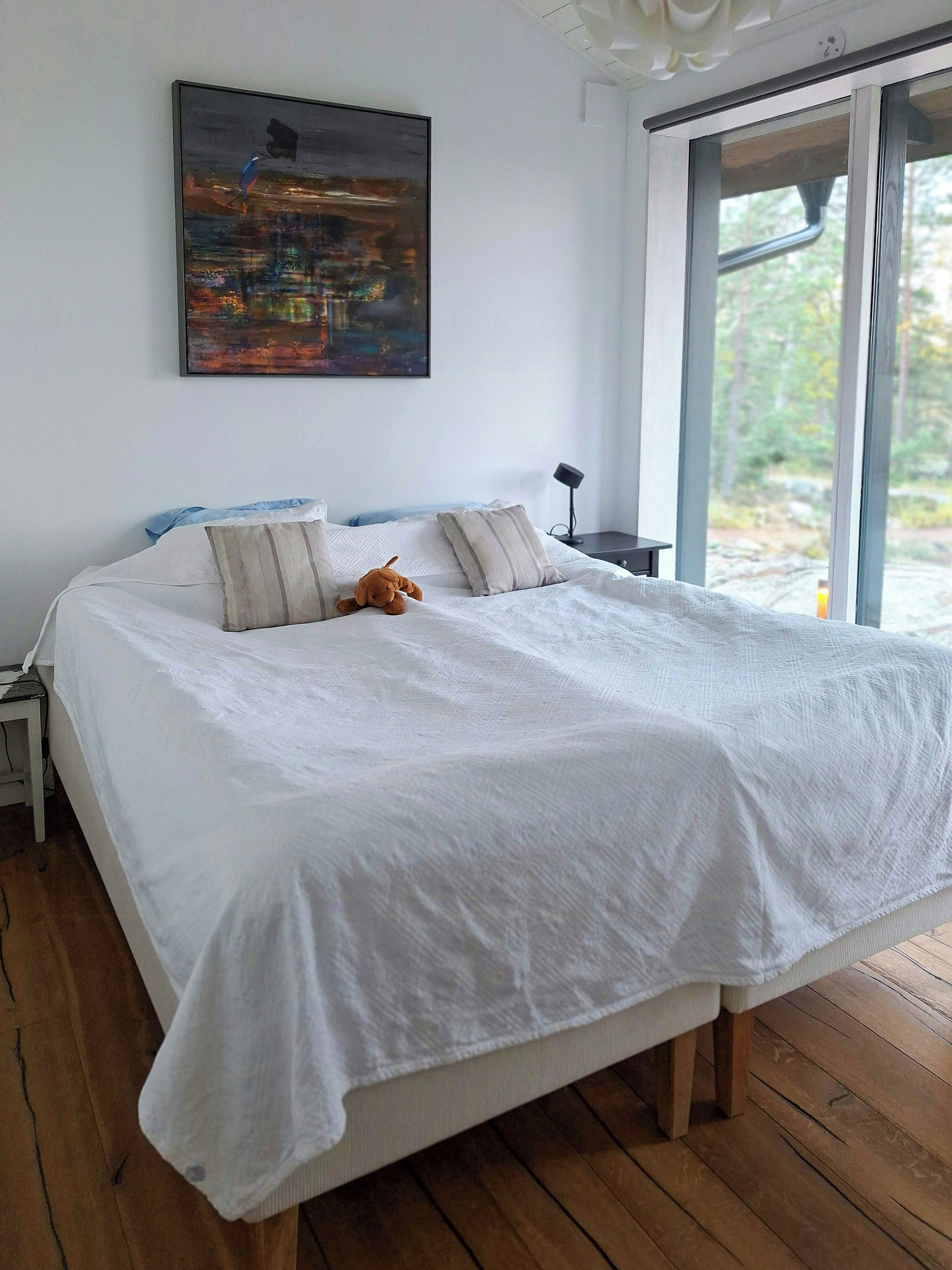 A bedroom with a large bed, a nightstand, a lamp, and a painting on the wall.
