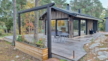 A modern cabin with a deck, a dining area, and a large window.