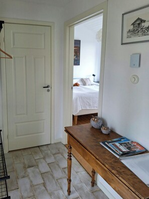 A hallway with a wooden table, a white door, and a bed in the background. - Seaside Guesthouse with terrace in Gustavsberg (Stockholms län)