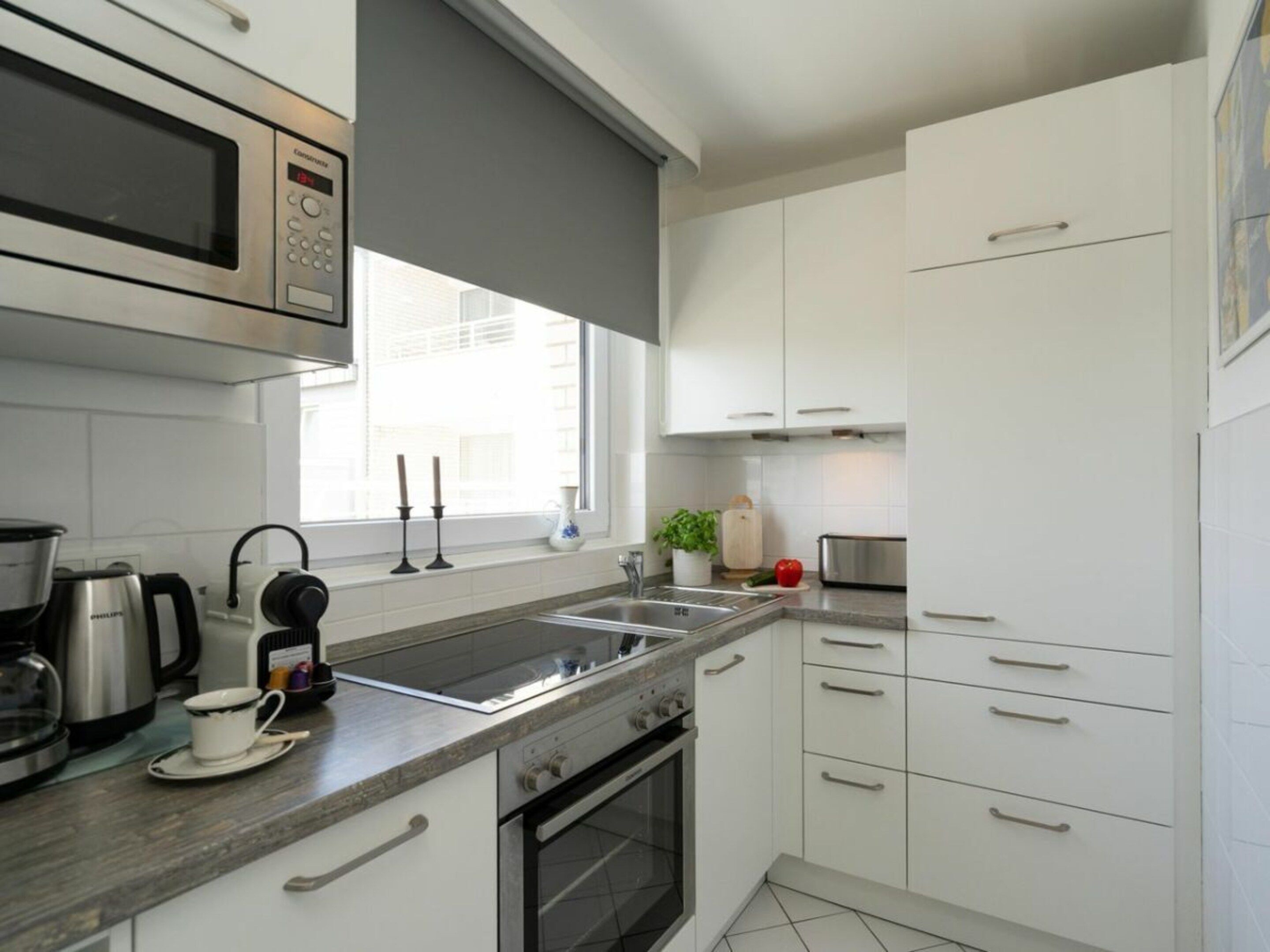 A modern kitchen with white cabinets, a stainless steel microwave, a coffee maker, and a toaster.