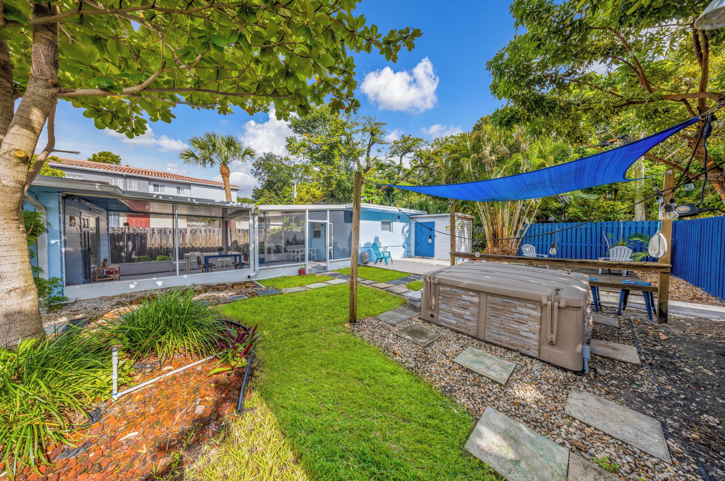 A residential property with a covered outdoor seating area, a patio, and a backyard with a lawn and trees.