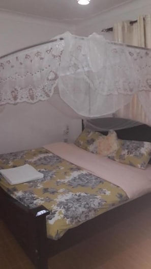 Una cama con colcha estampada de flores, un almohadón blanco y un dosel con detalles de encaje.