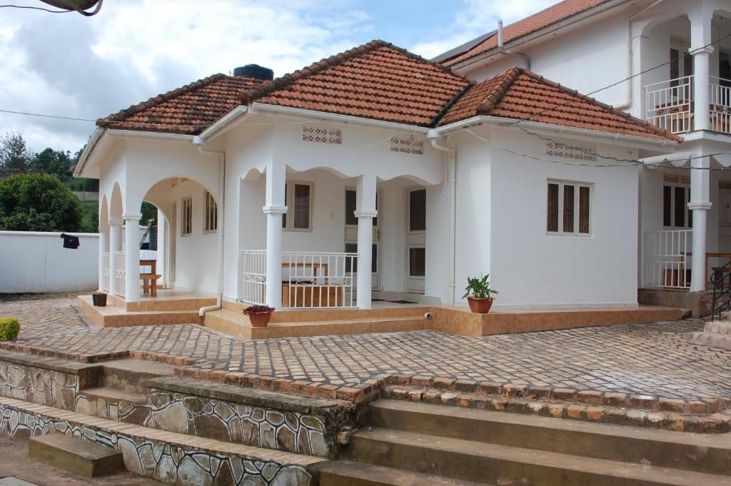 A two-story house with a tiled roof, a covered porch, and a paved front yard.