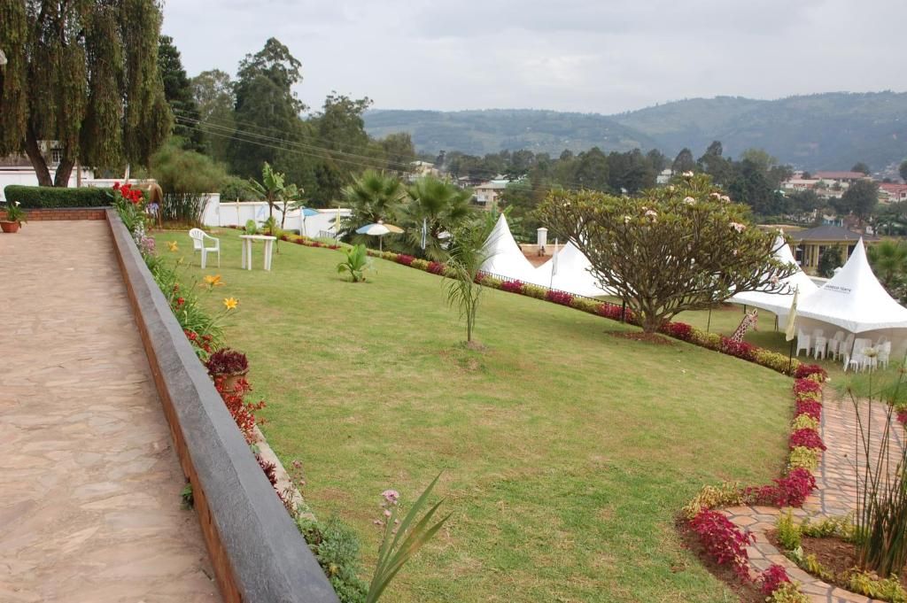 A well-maintained lawn with a white tent structure, surrounded by a variety of plants and a clear view of distant hills.