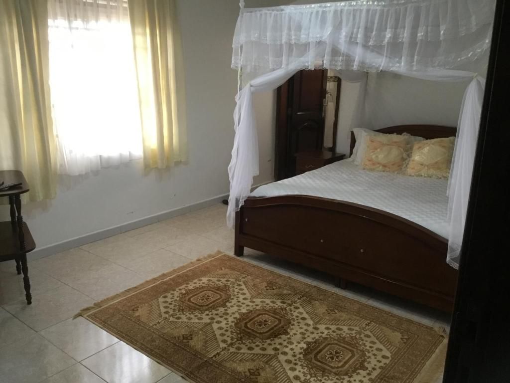 A bedroom with a bed, a nightstand, a bedside table, a patterned rug, and a window with curtains.