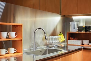 A modern kitchen with a stainless steel sink, wooden cabinets, and a glass display shelf with white mugs. - Gem Hostel Seoul (jung-gu)